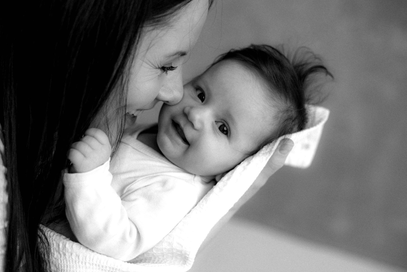Tender moment between a smiling mother and baby in a cozy, intimate setting.